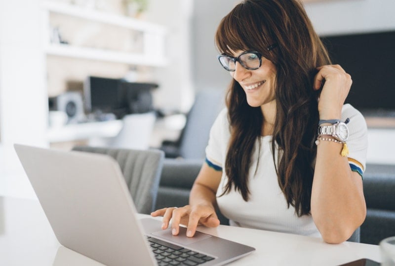 Smiling woman sat behind a laptop interacting with it using her right hand.